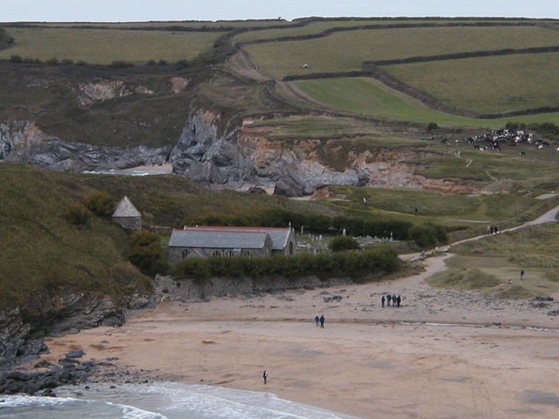 Looking across a beach to a small church, the tower seems to be half buried in the hillside