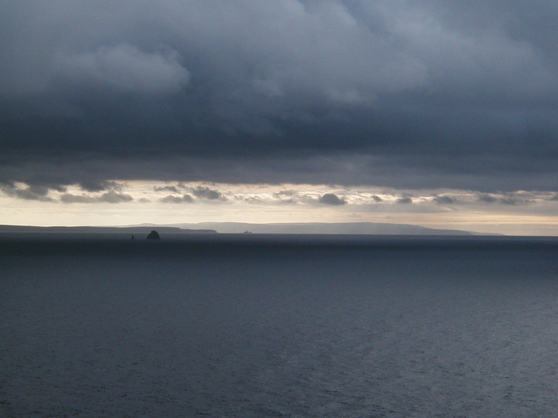 Dark grey clouds over the sea, outline of coastline in the distance.
