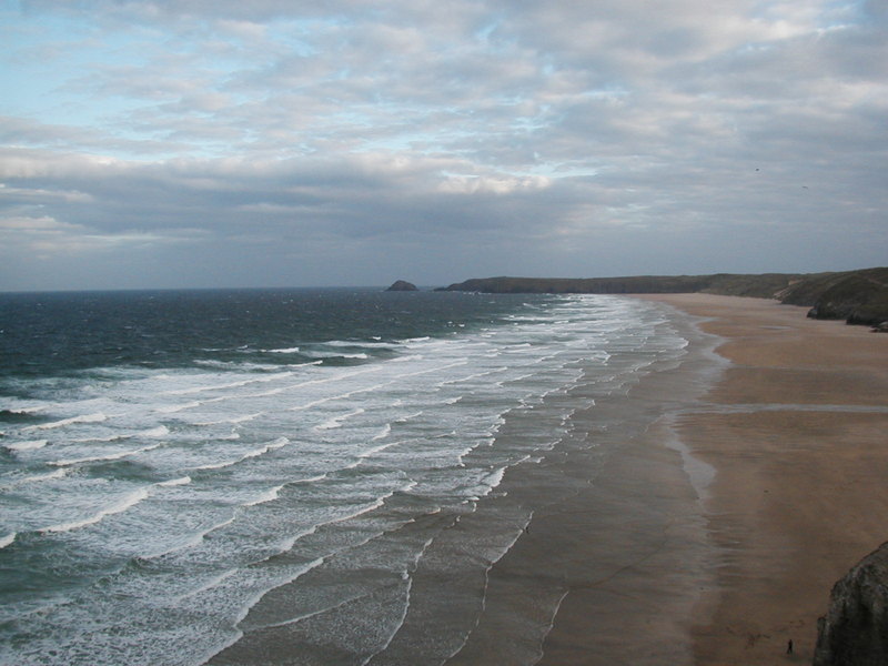 View along beach, lots of white surf rolling in.