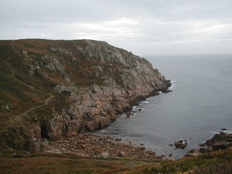 Looking out to a headland, steep granite blocks running down to the sea, the path meandering through the heather above.