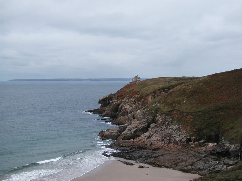 Small house on a headland of rocky granite with steep grass and fern covered hillside above.