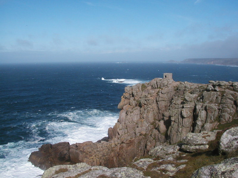Rugged granite cliffs with tiny stone lookout building on top, sea in background