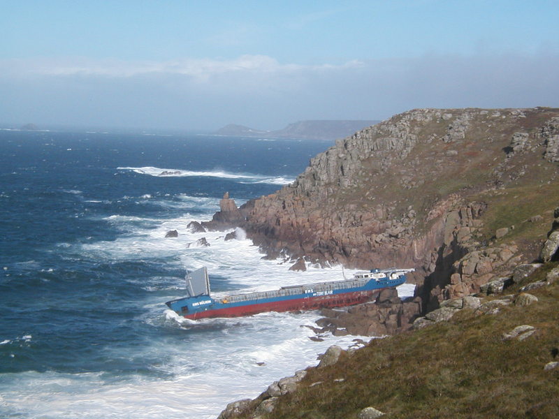 Looking down on large red and blue tanker grounded on rough brown granite coast.