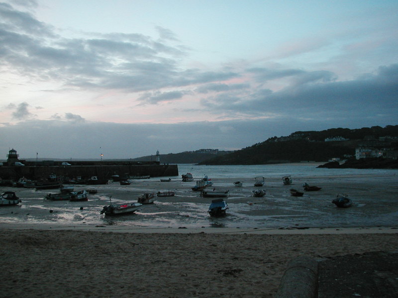 Looking out at pier and boats resting on sandy beach at low tide, in early morning light