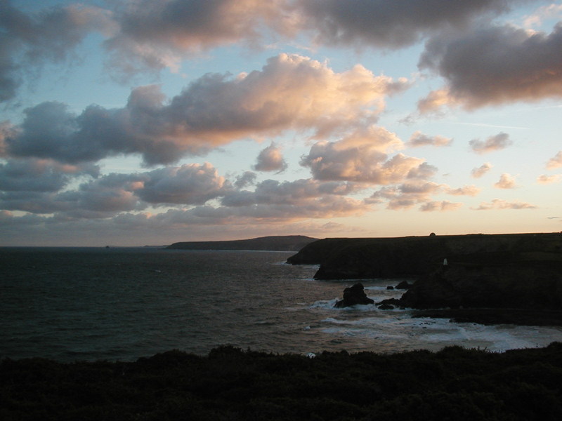 Cliffs and sea stretching off into distance, only just light, sky scattered with clouds with pink tinge