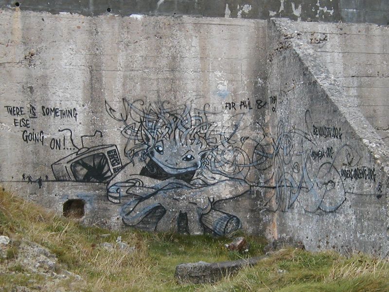 Graffiti on wall, of smiling face, holding a hammer, and smashed TV set in the background.