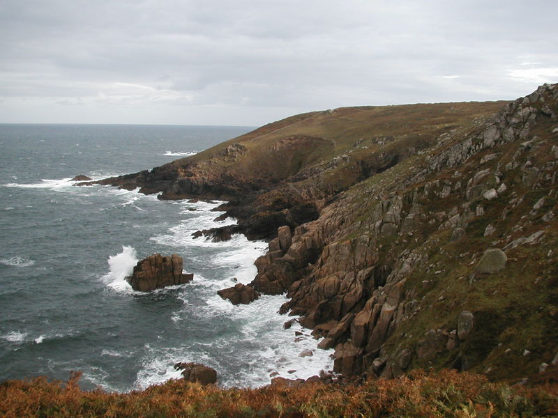 Coastline of rugged brown granite with choppy sea below and lots of white spray.