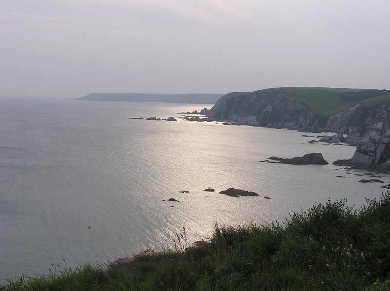 Headland with slabby cliffs leading down to shoreline, evening sun reflecting off the sea.