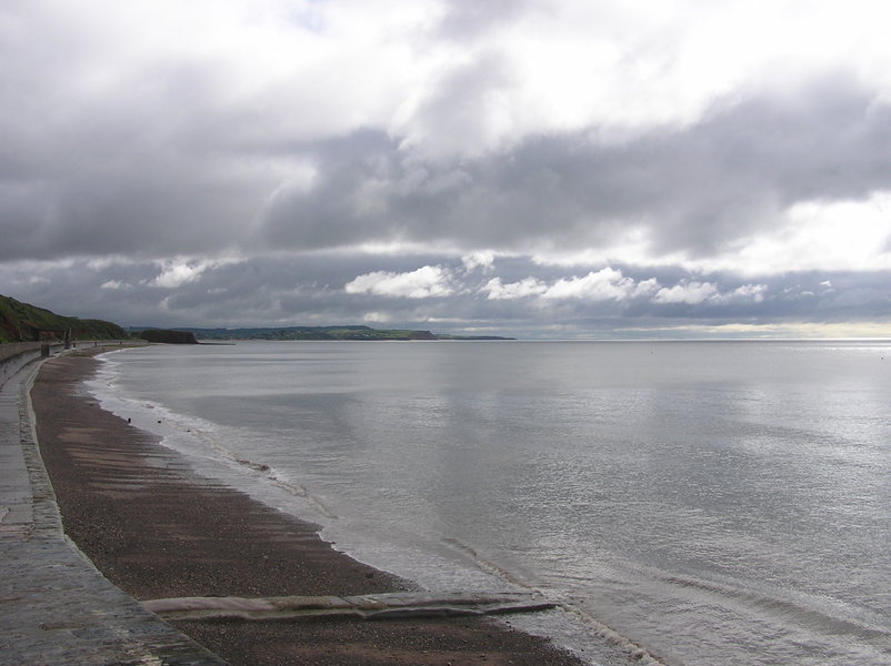 View along seawall, grey clouds, and grey sea.