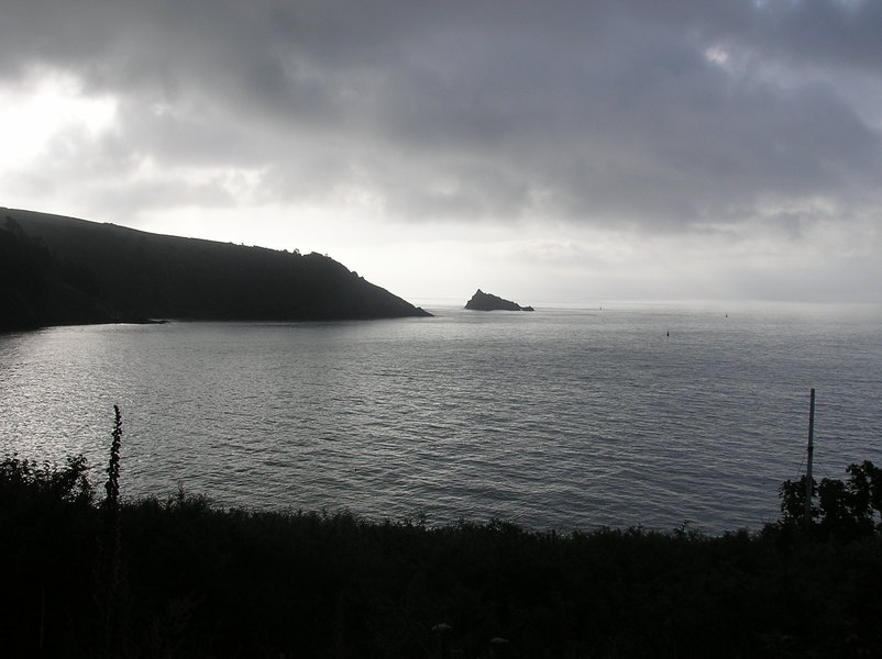 Very dark view across grey sea to silhouetted headland and small island on other side.
