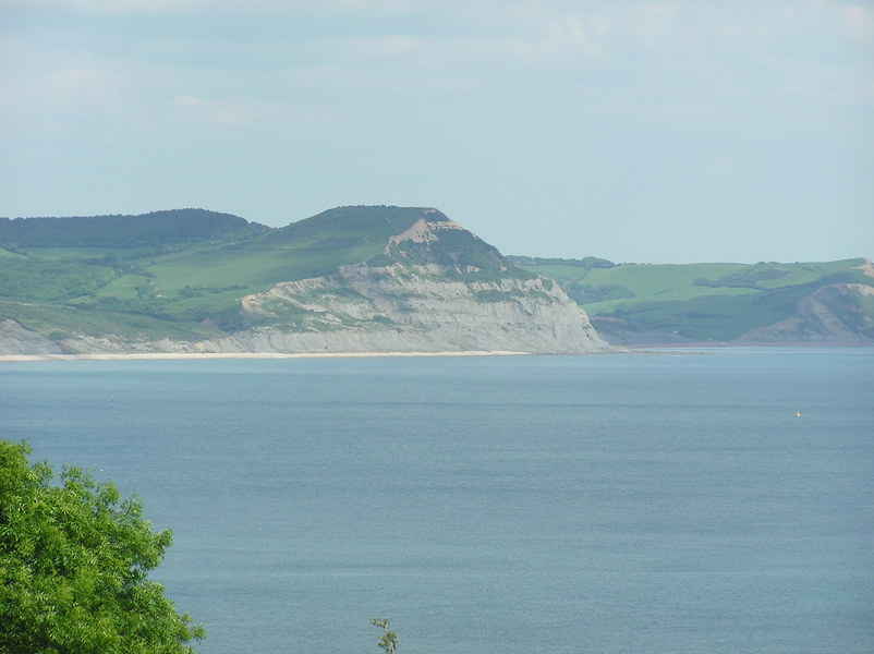 View across the sea to small peak, with triangular cliff leading down to the sea.