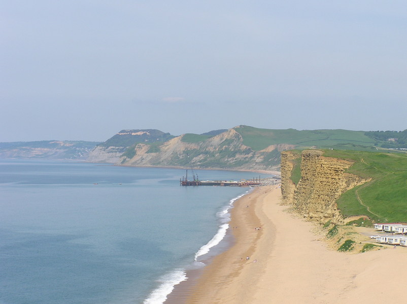 View out along beach, past crumbling yellow cliffs towards larger hills in the distance.