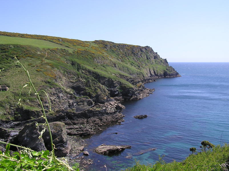 Looking out towards headland, craggy cliffs, grass and gorse on top, clear blue sky.