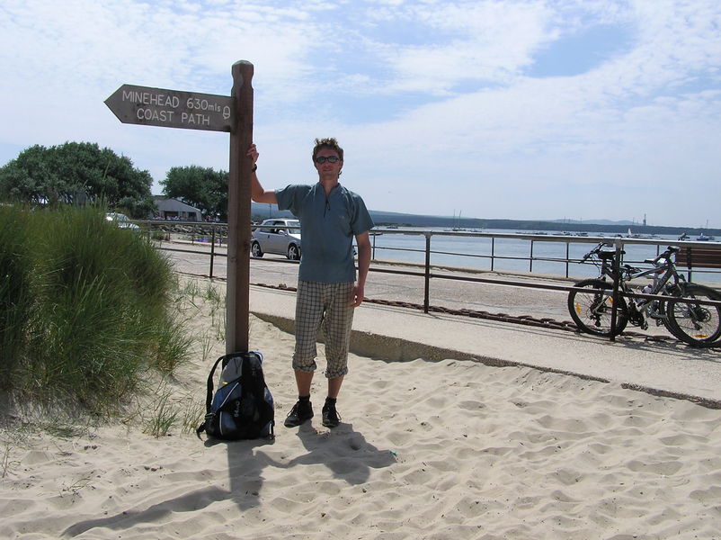 me standing on beach by sign that says 'Minehead 630mls, Coast Path'.