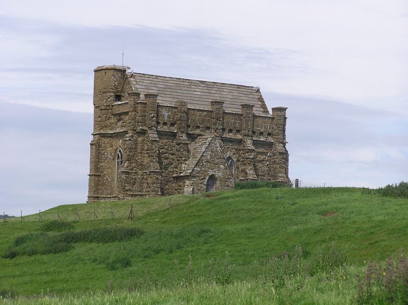 Small brown turreted church on top of grassy hilltop.