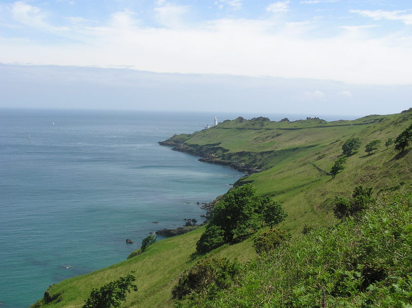 Sun covered grassy hillside stretching down to small white lighthouse.