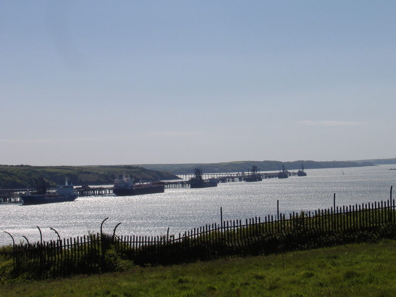 Looking out across a stretch of water, with 6 large tankers moored up in a line against a jetty